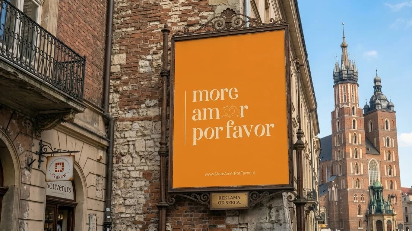 Pomarańczowy szyld w kutej ramie na krakowskiej kamienicy z napisem „more amor por favor” i serduszkiem z dłoni, a w tle bazylika Mariacka